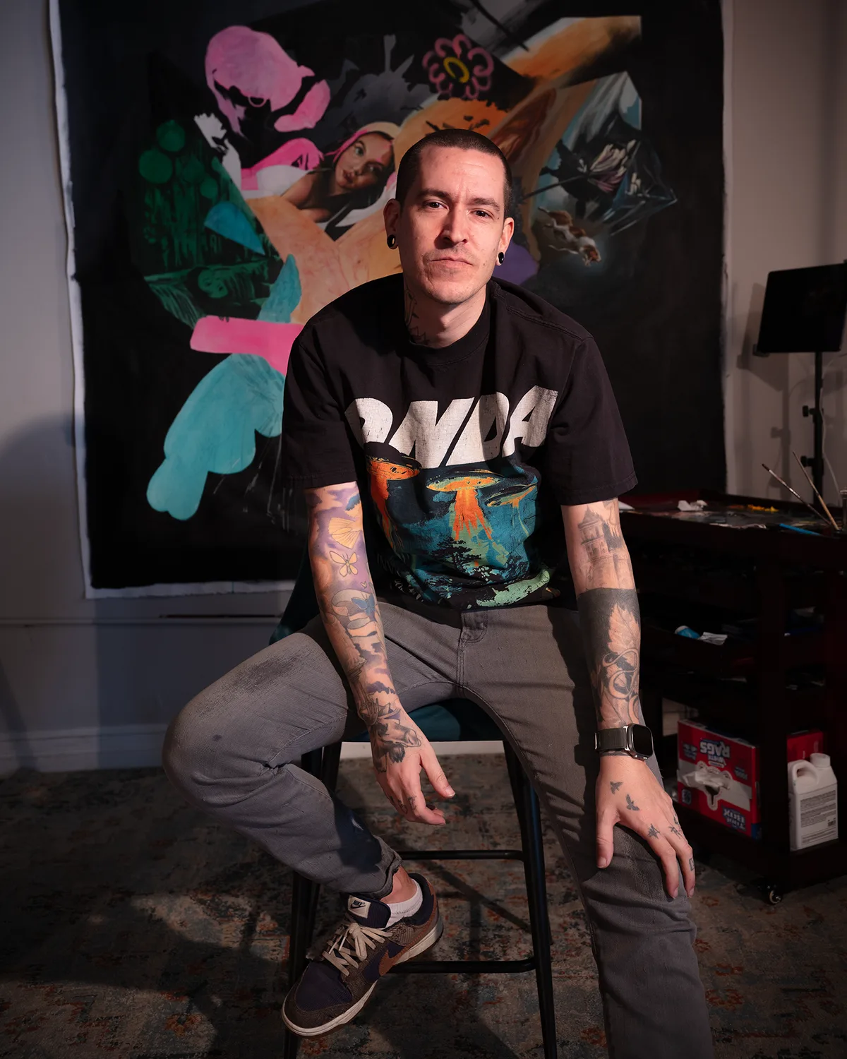 Wetiko seated on a stool in his studio in front of a large painting