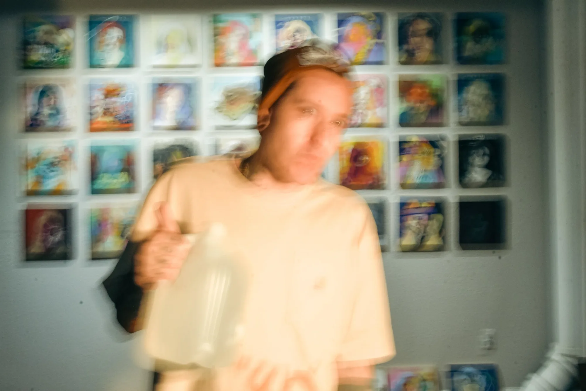 Wetiko holding a bottle in front of a wall of Edith and Lover paintings